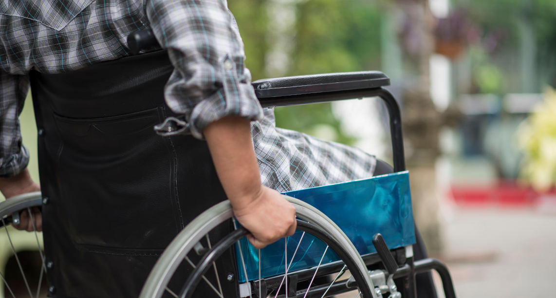 Close-up of senior woman hand on wheel of wheelchair during walk